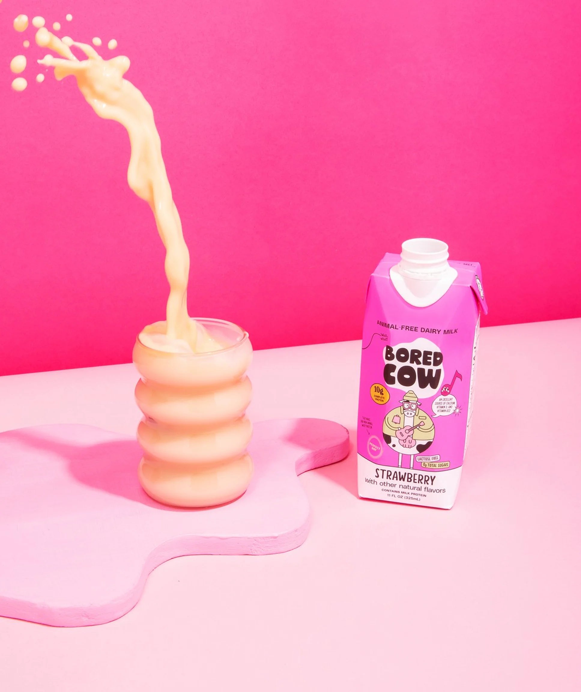 Bored Cow strawberry milk being poured into a glass with a pink background
