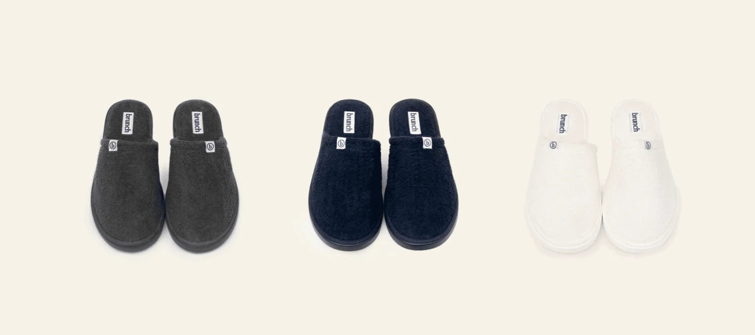 Three pairs of slippers in black, navy, and white on a light beige background.