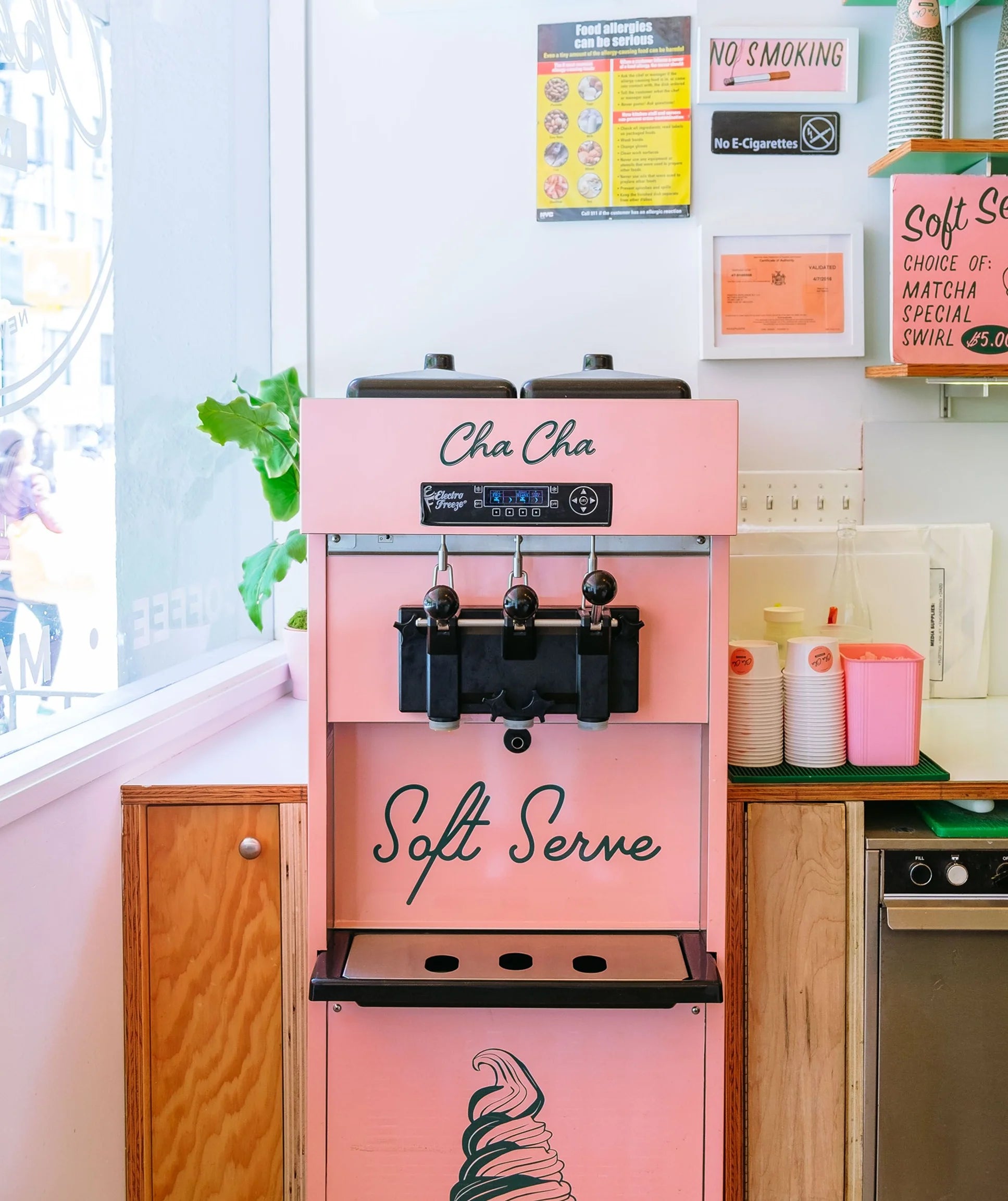 Pink soft serve ice cream machine in a kitchen setting with posters on the wall.