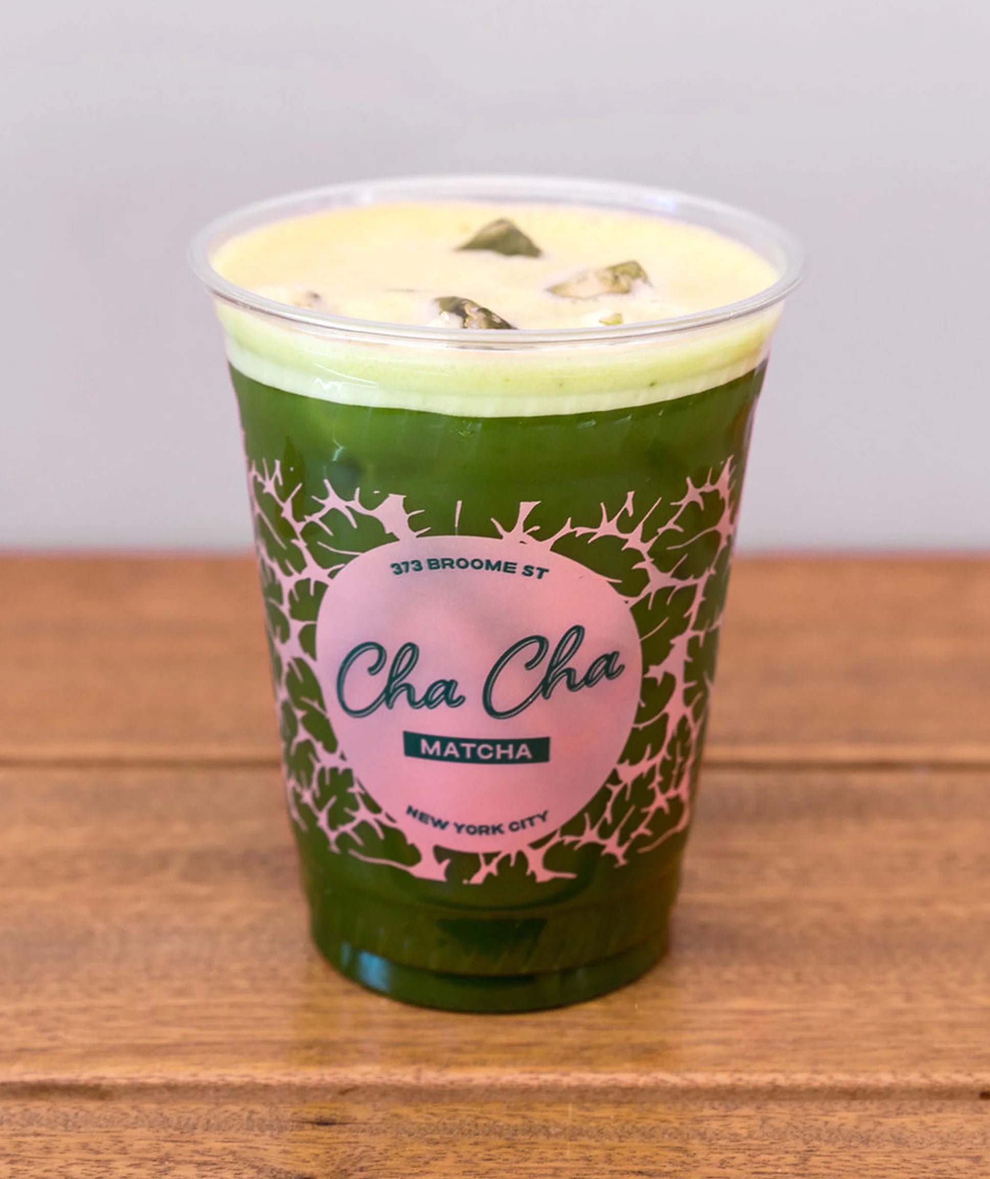 Green matcha drink in a cup with 'Cha Cha' branding on a wooden surface.