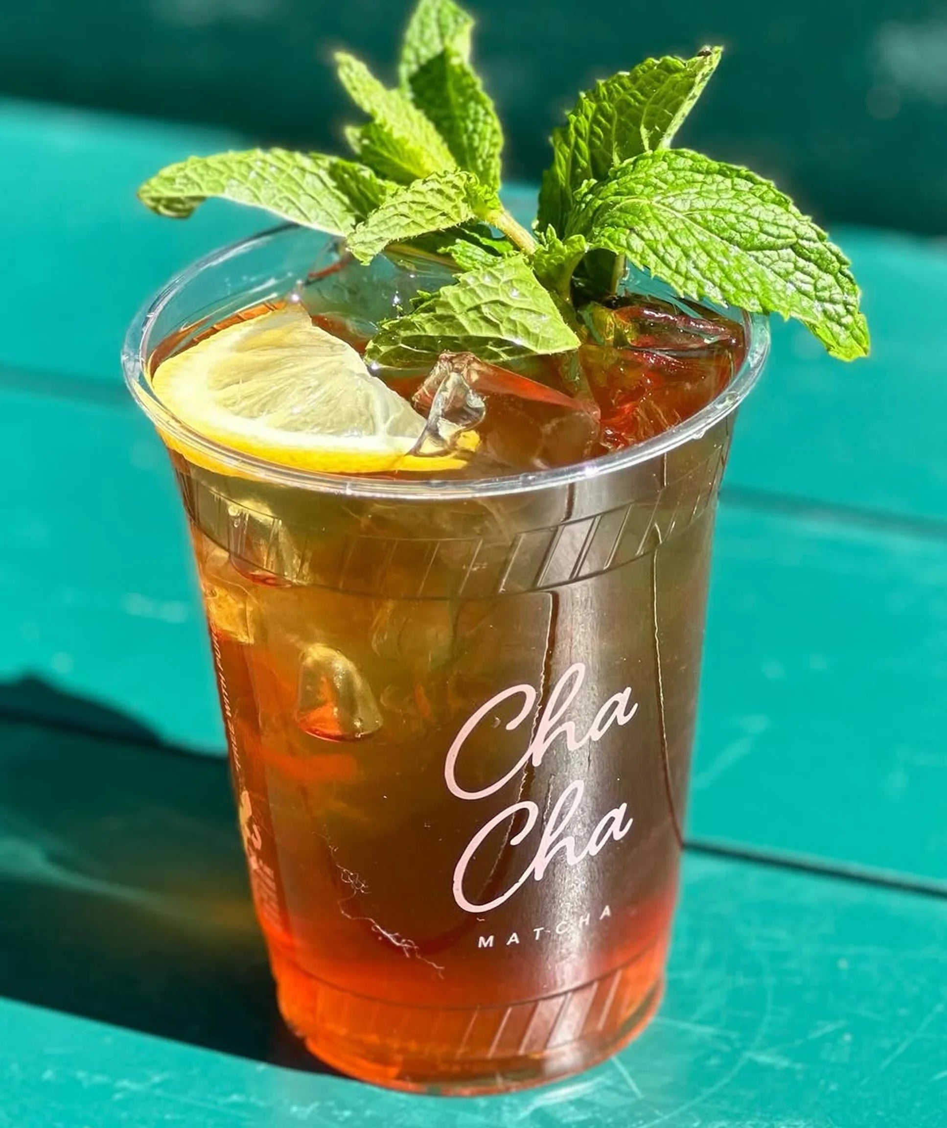 Glass of iced tea with lemon and mint leaves on a teal background