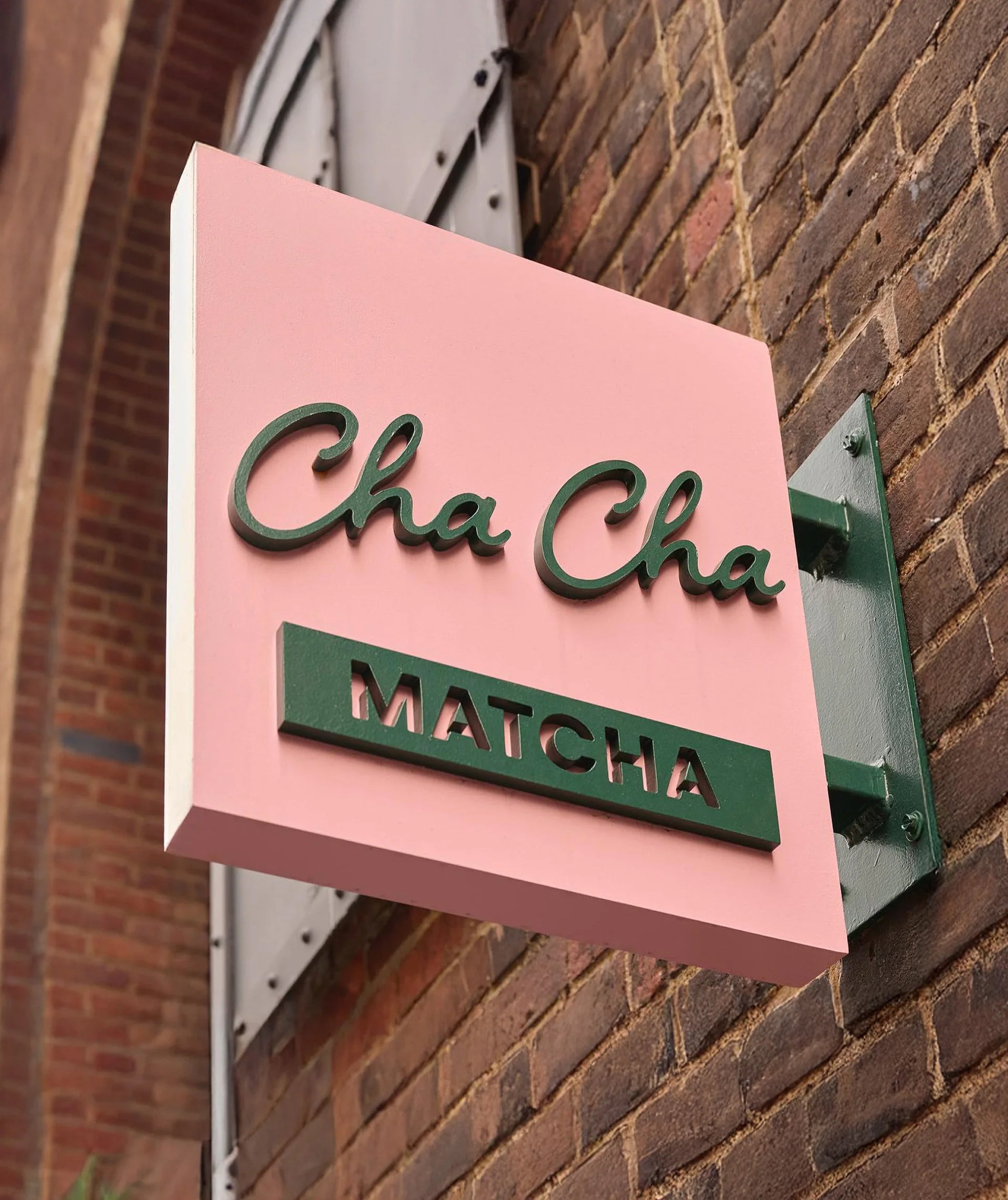 Pink and green sign for 'Cha Cha Matcha' on a brick wall.