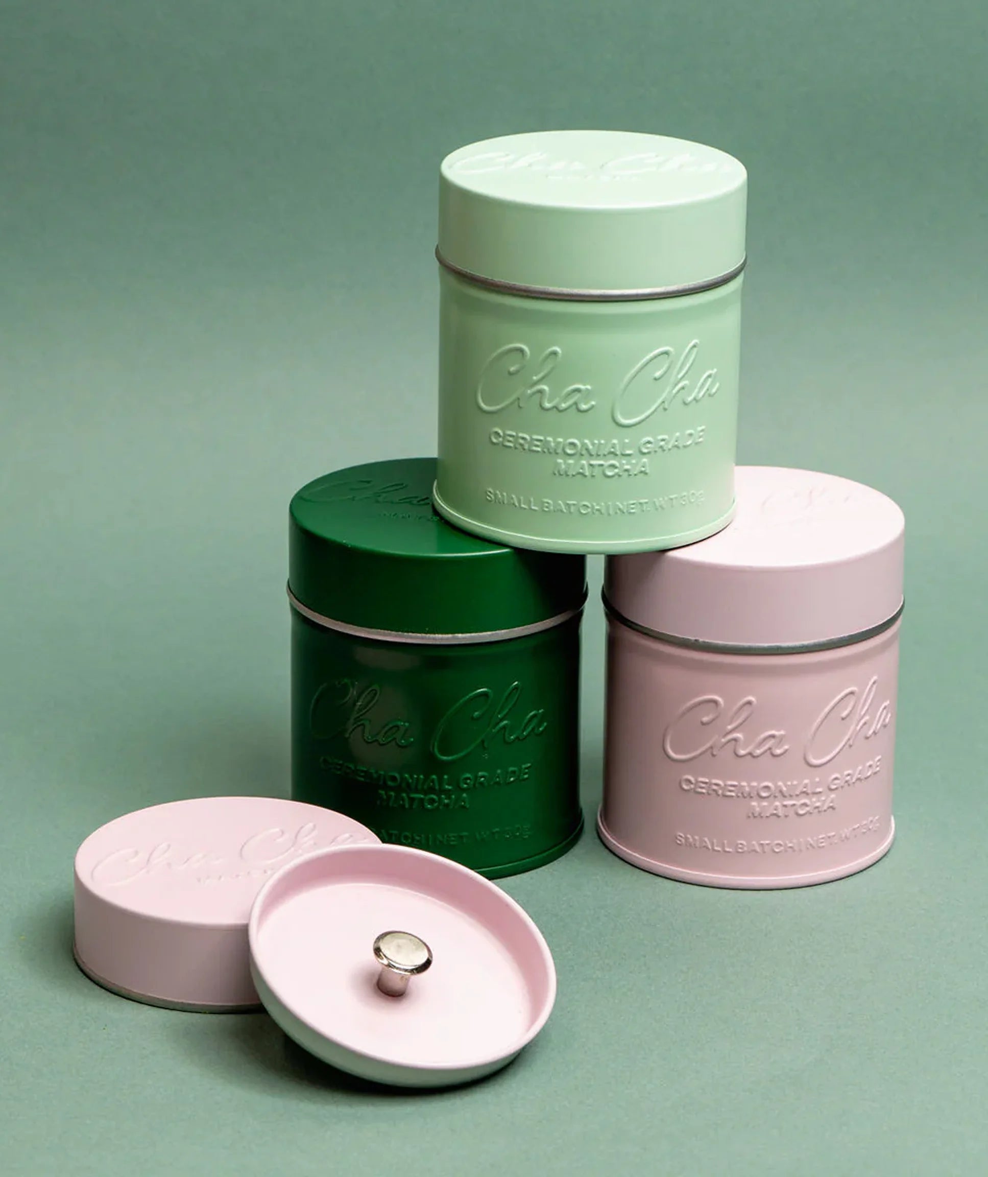 Three cylindrical containers with lids, branded 'Cha Cha', on a green background.