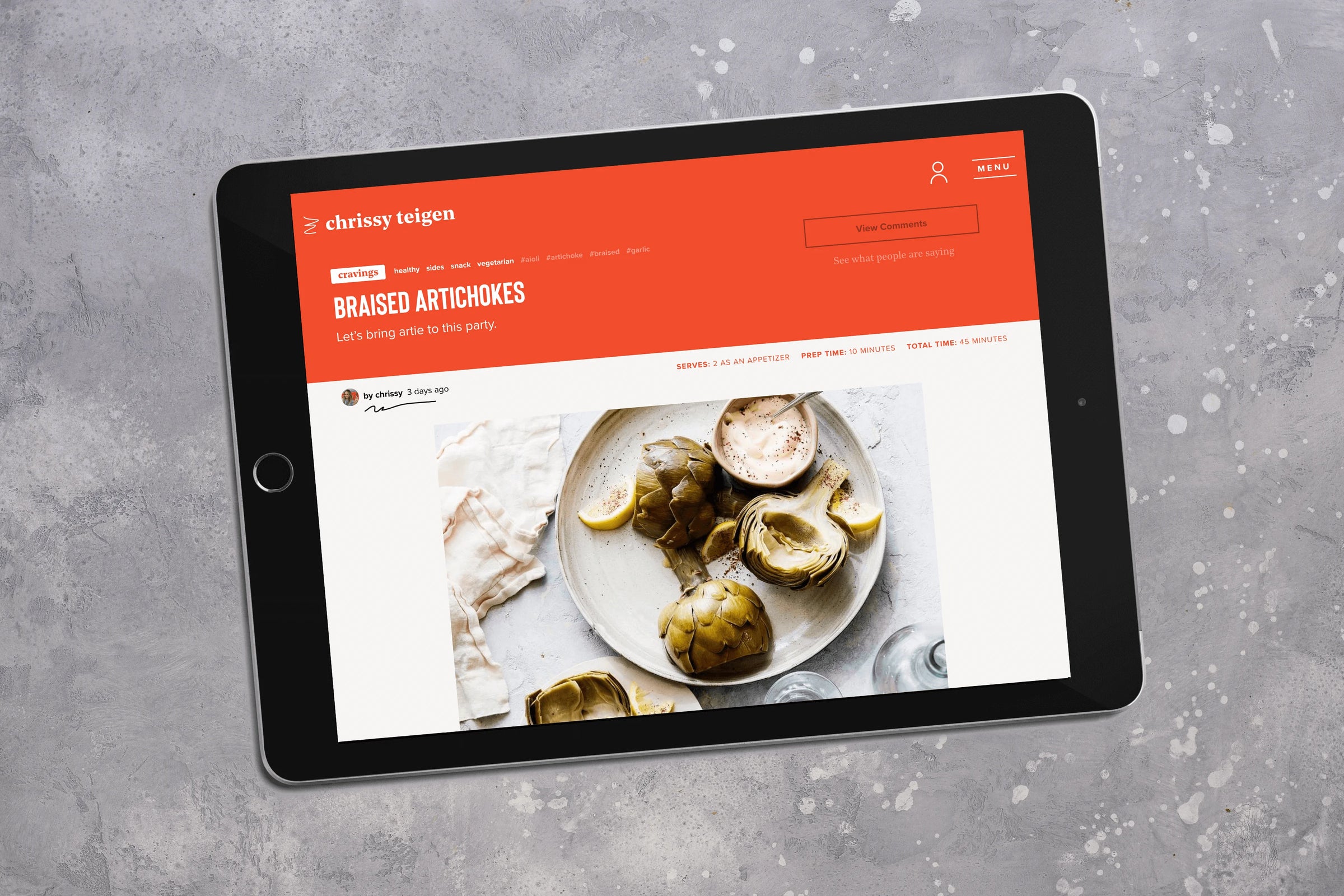 Tablet displaying a recipe for braised artichokes on a gray surface