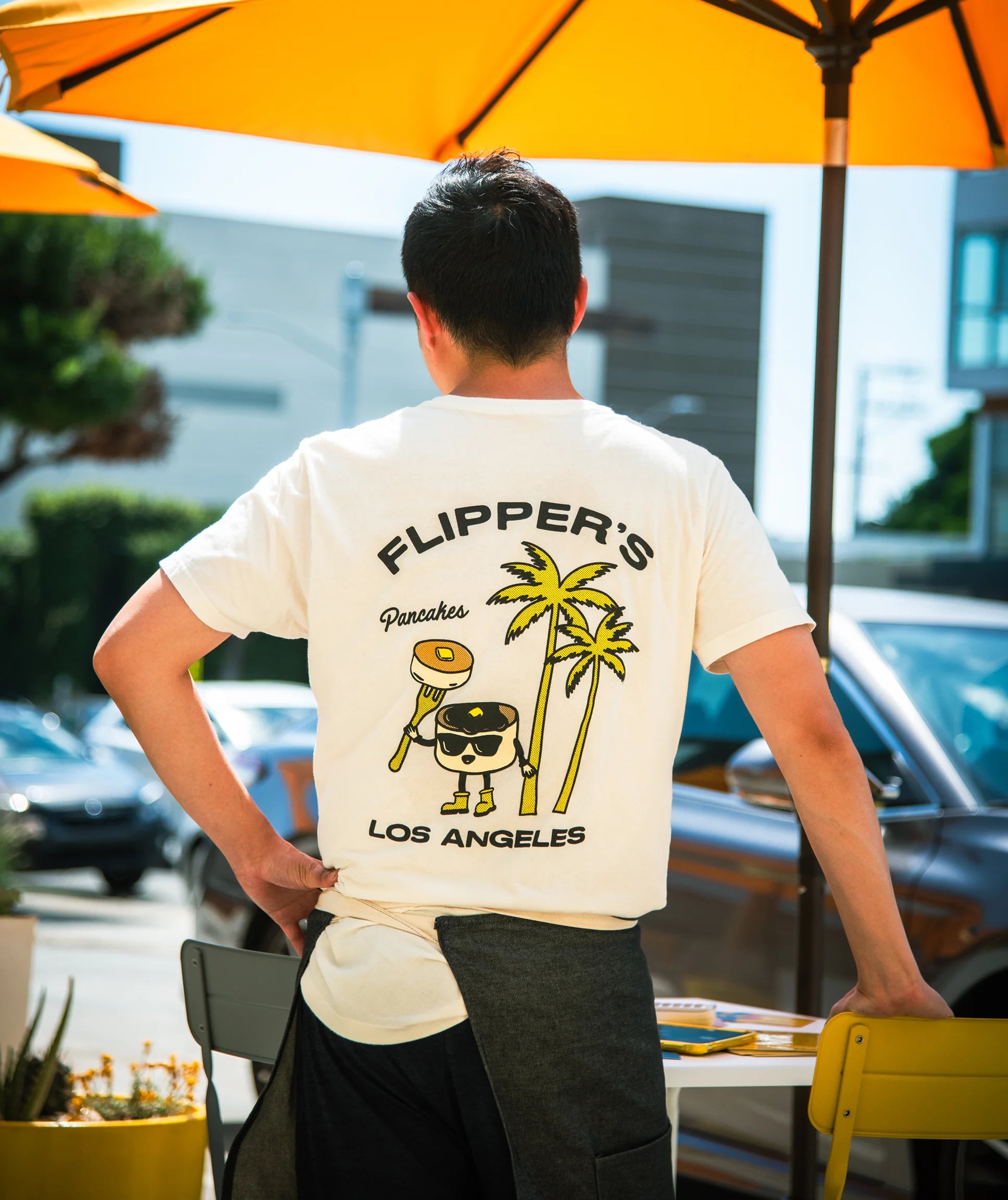 Person wearing a t-shirt with 'Flipper's' branding and palm tree design outdoors.