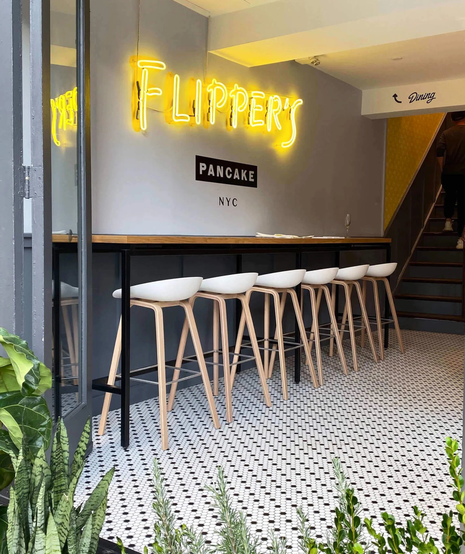 Neon sign reading 'Flipper's Pancake NYC' above a row of stools in a modern interior.
