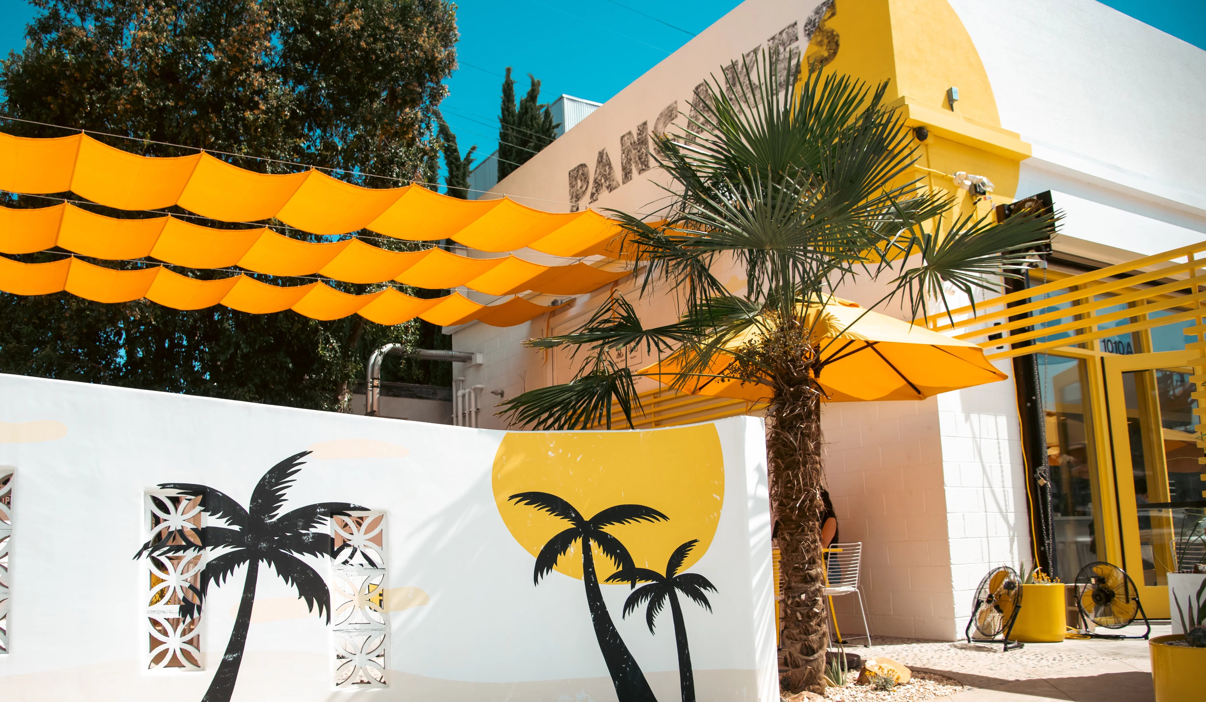 Outdoor setting with yellow canopy, palm tree, and decorative pillows featuring palm trees.