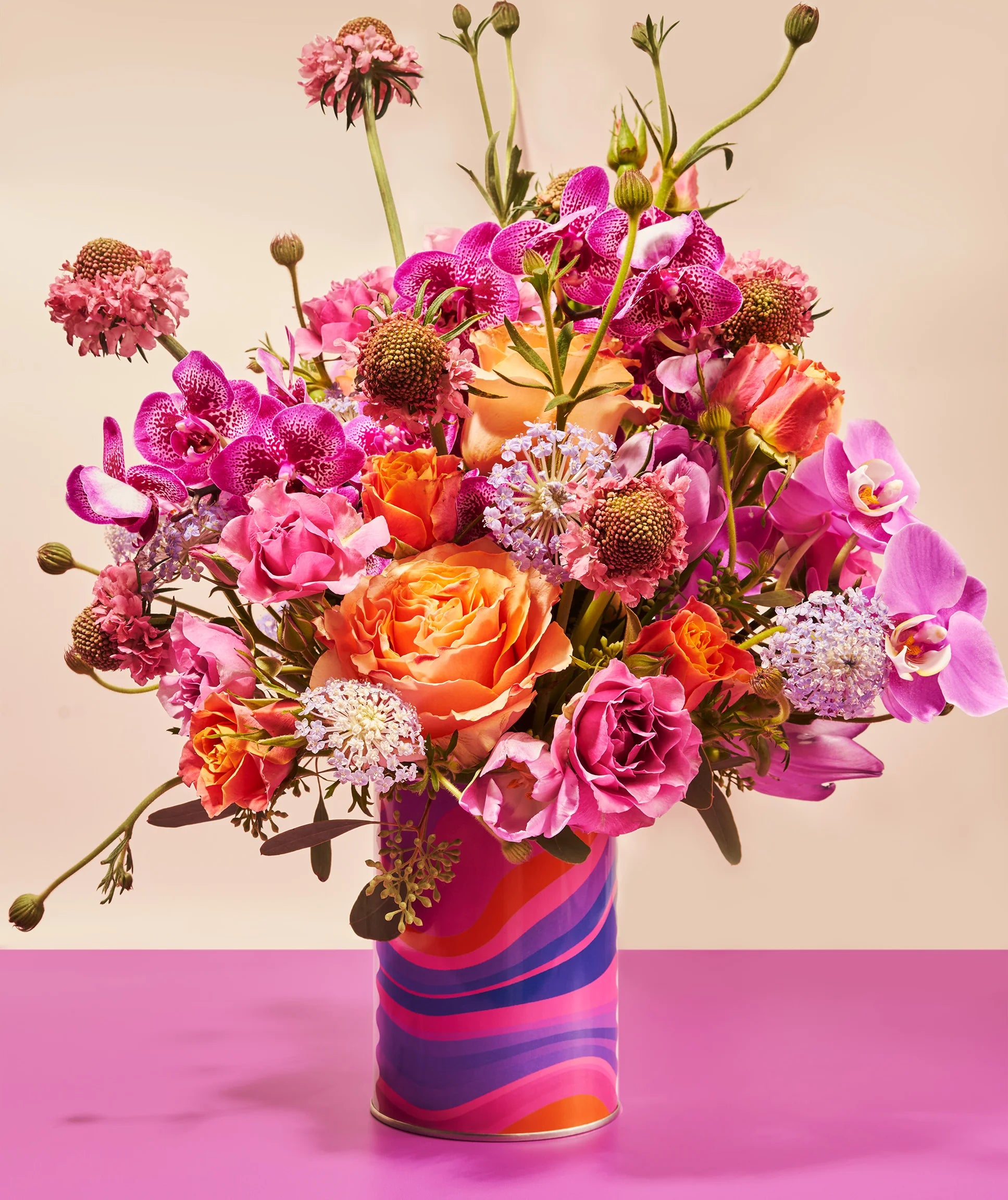 Colorful bouquet of flowers in a striped vase on a pink background