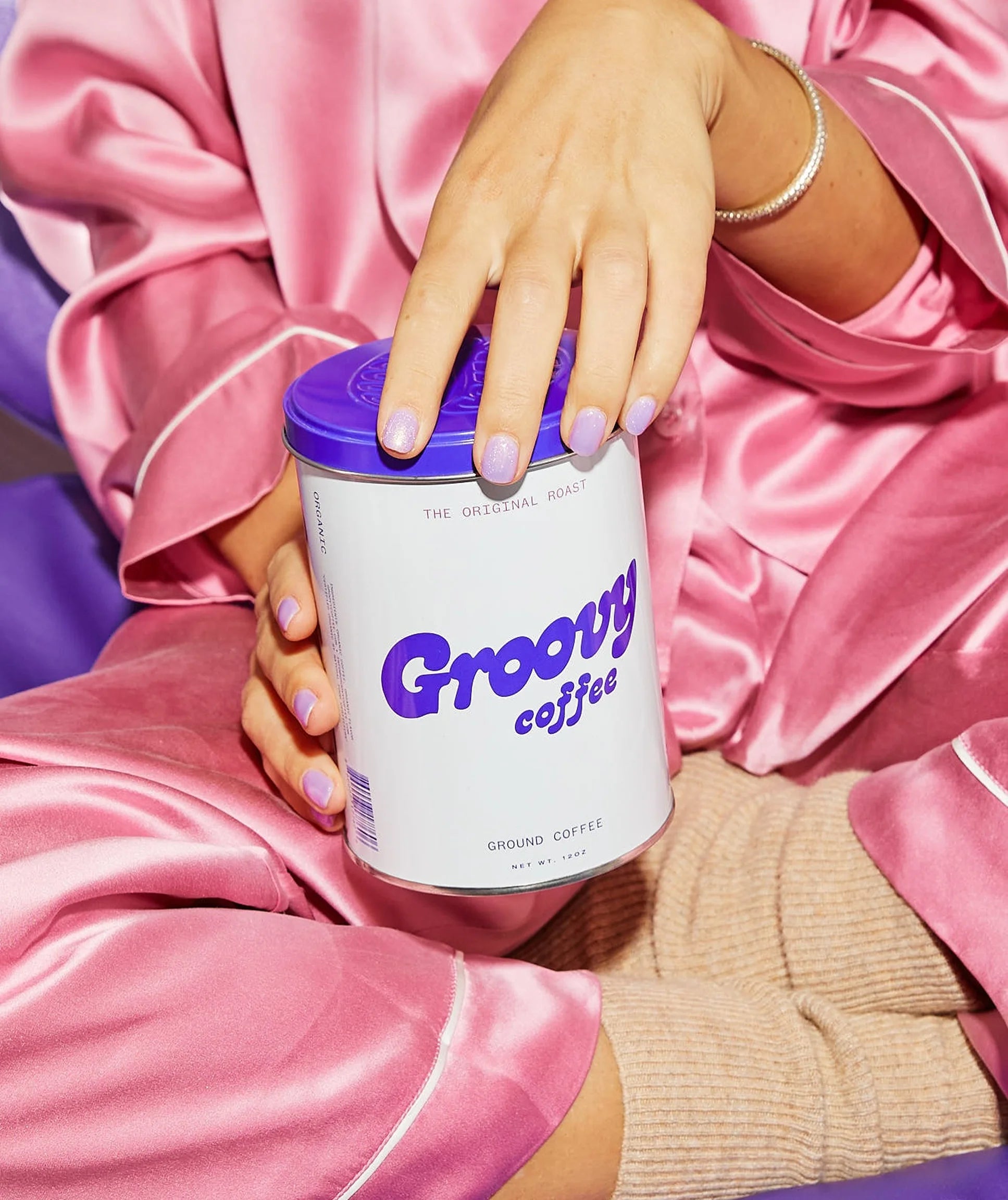 Person holding a can of Groovy Coffee in pink satin pajamas.