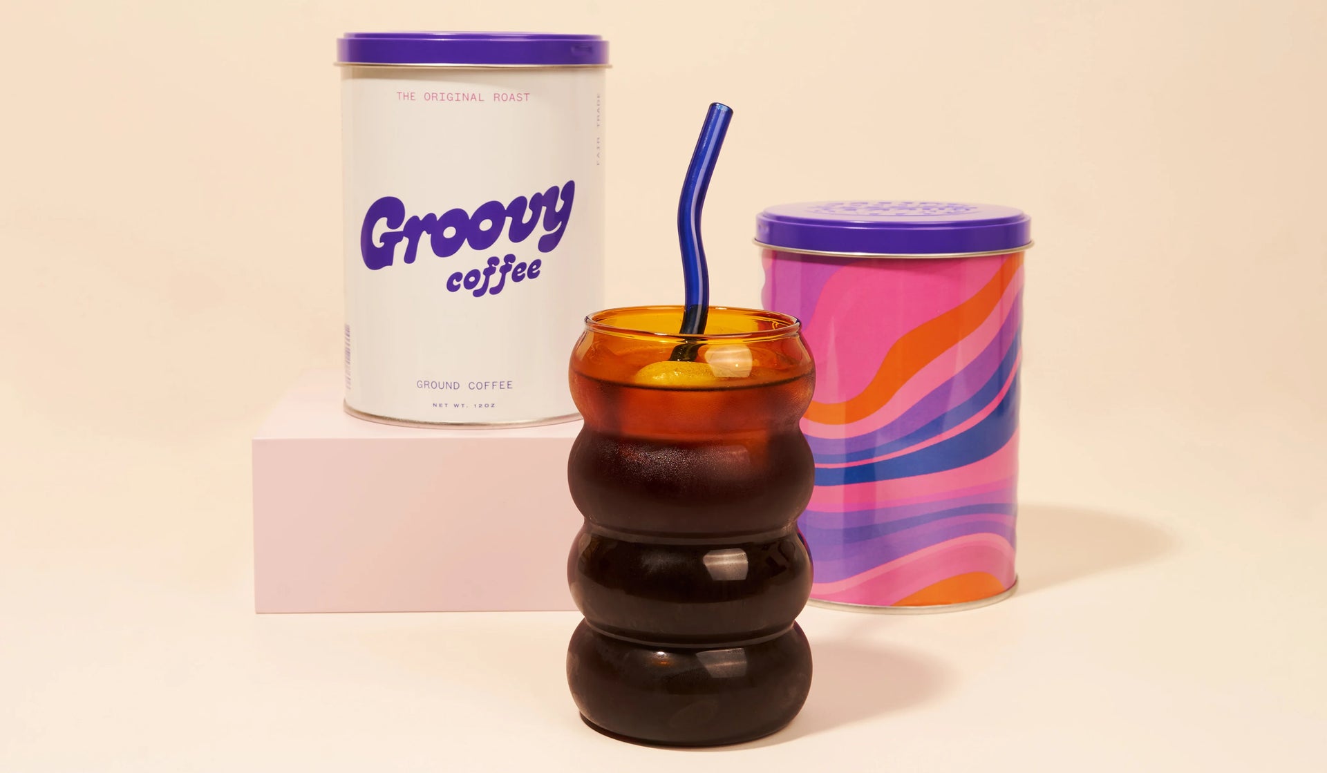Colorful coffee cup with a straw, canister labeled 'Groovy Coffee', and marbled-patterned container on a beige background.