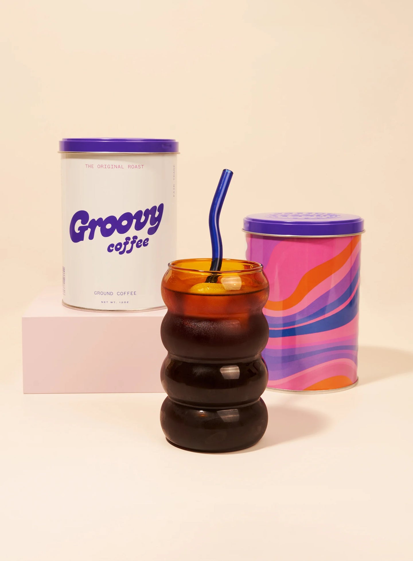 Colorful coffee cup with a straw, 'Groovy Coffee' container, and marbled container on a beige background