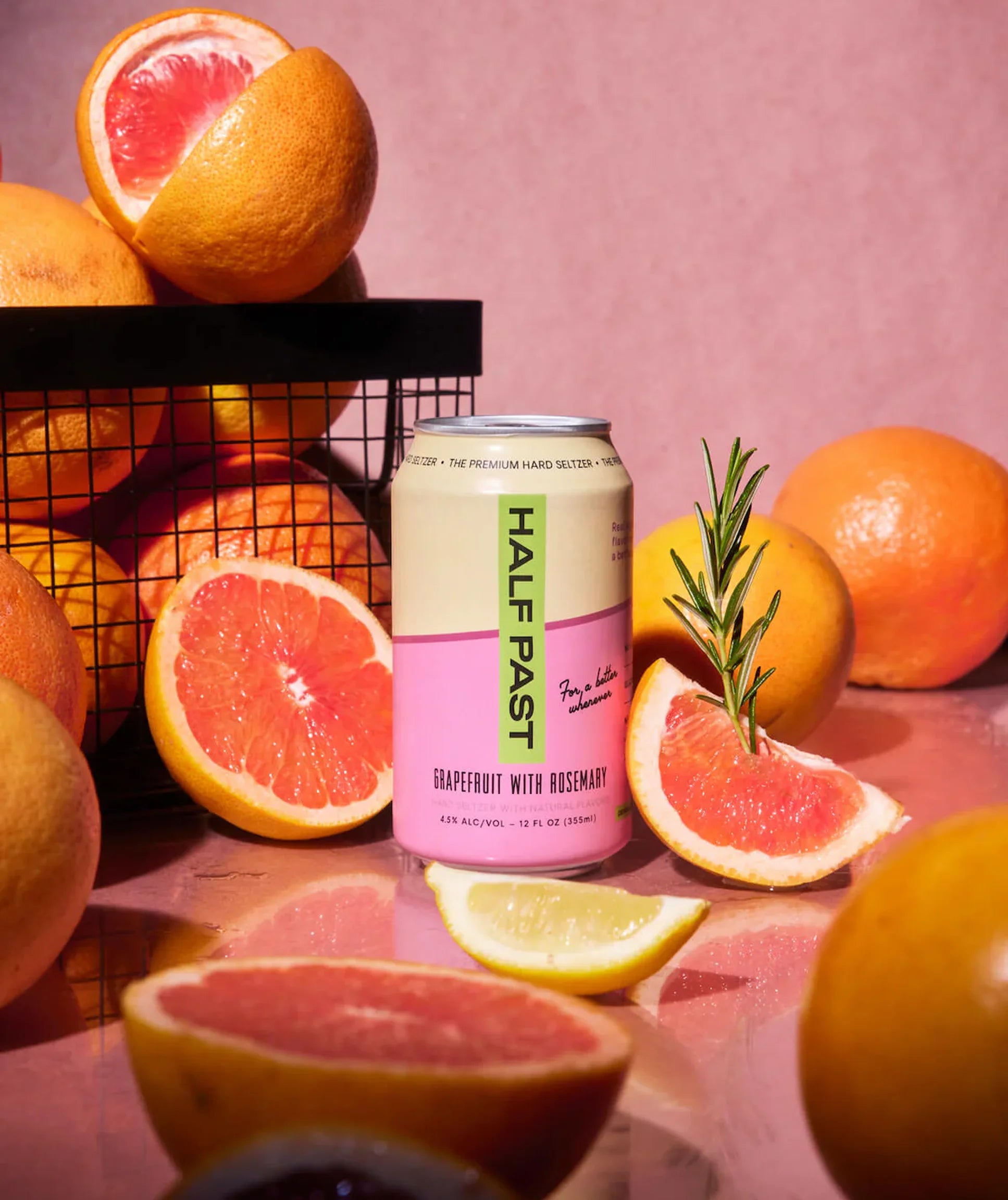 Can of 'Half Past' grapefruit with rosemary beer surrounded by sliced oranges and lemons on a pink background