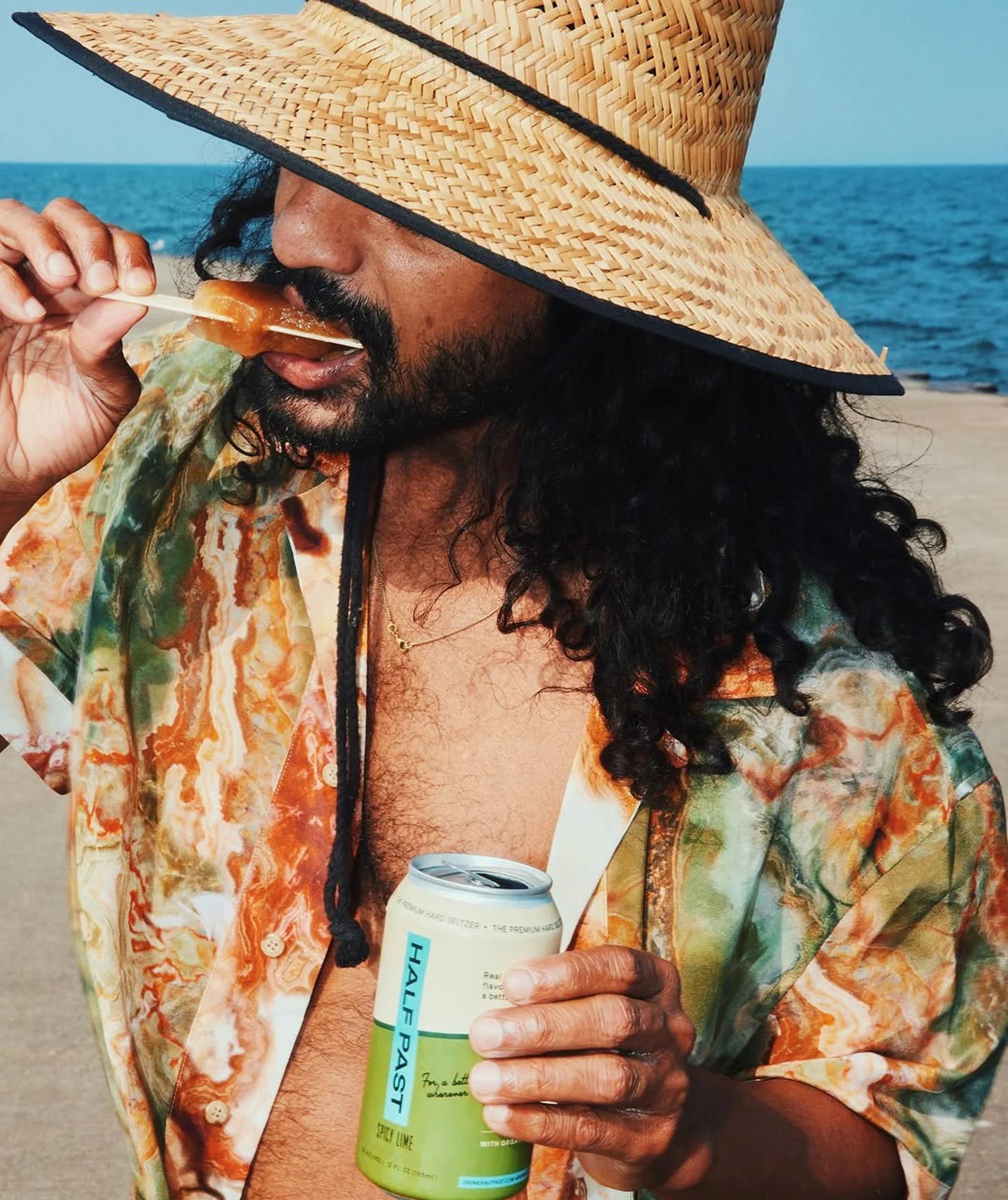 Man in straw hat and colorful shirt enjoying a beach day with a can of Half Fast beer.