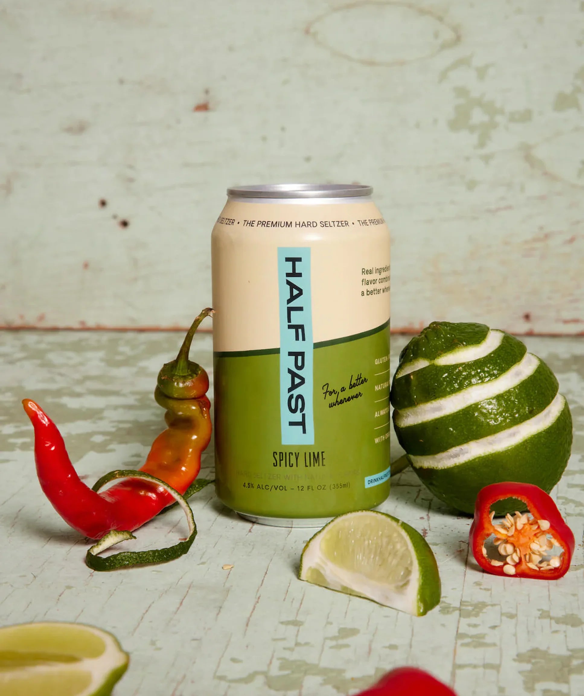 Can of Half Past Spicy Lime hard seltzer with limes and peppers on a textured surface