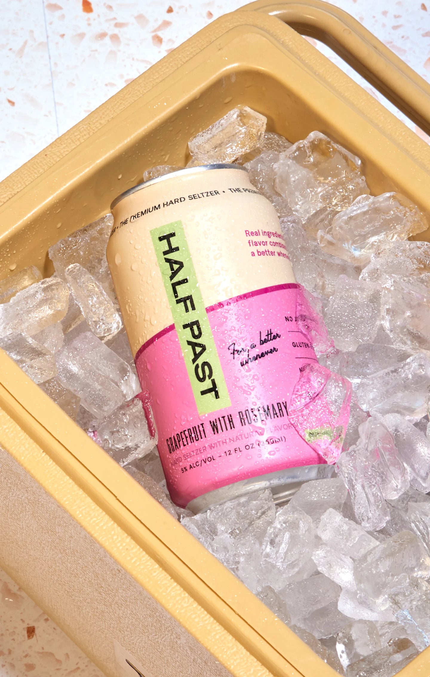 Pink and gold can of Half Past Hard Seltzer on ice cubes in a cooler.