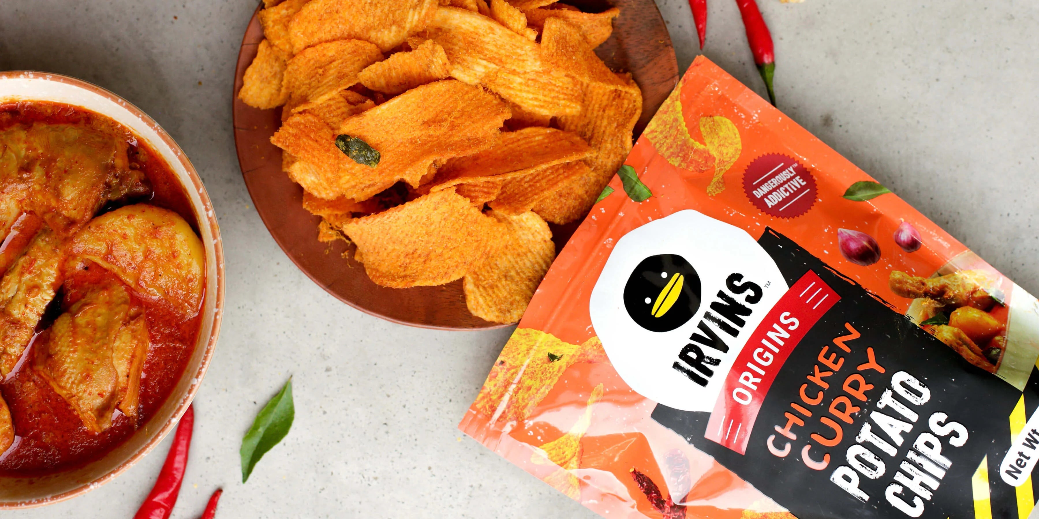 Irvins Origins Chicken Curry Potato Chips packaging with chips and dipping sauce on a table.