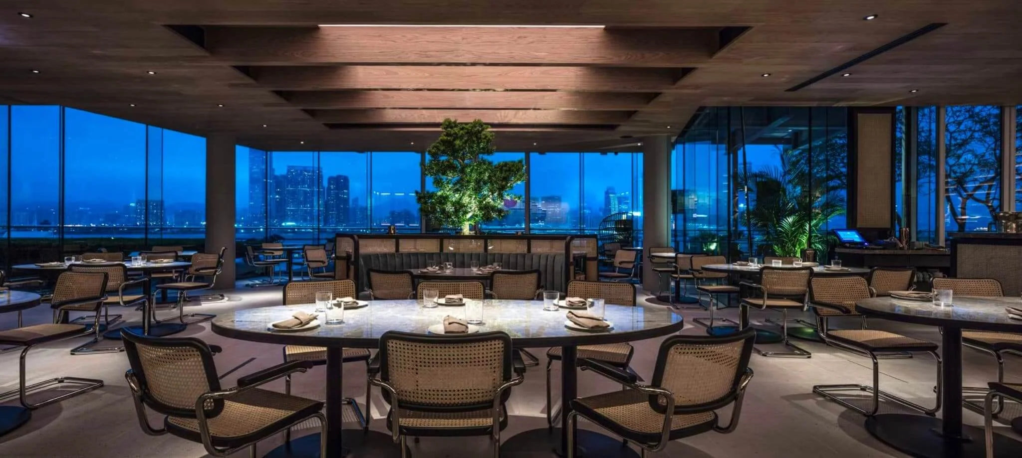 Modern restaurant interior with large windows overlooking a cityscape at night.