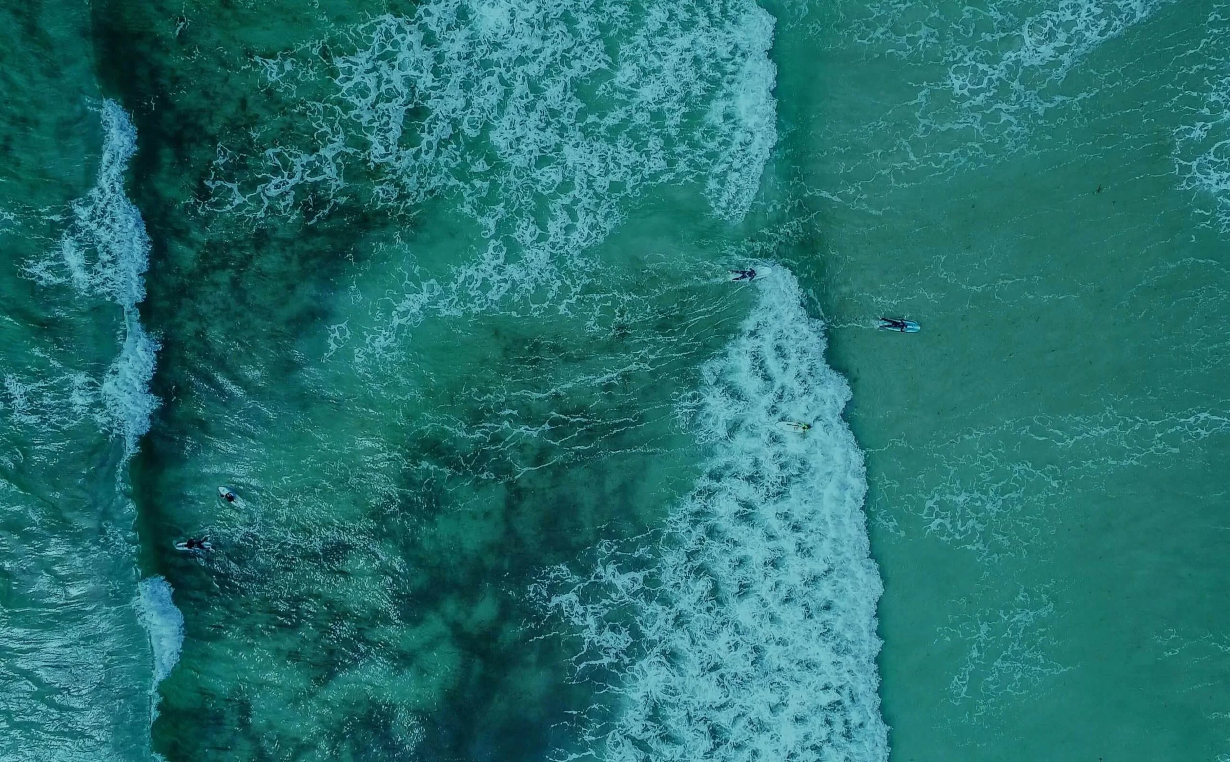 Aerial view of surfers paddling in the ocean with a large wave.