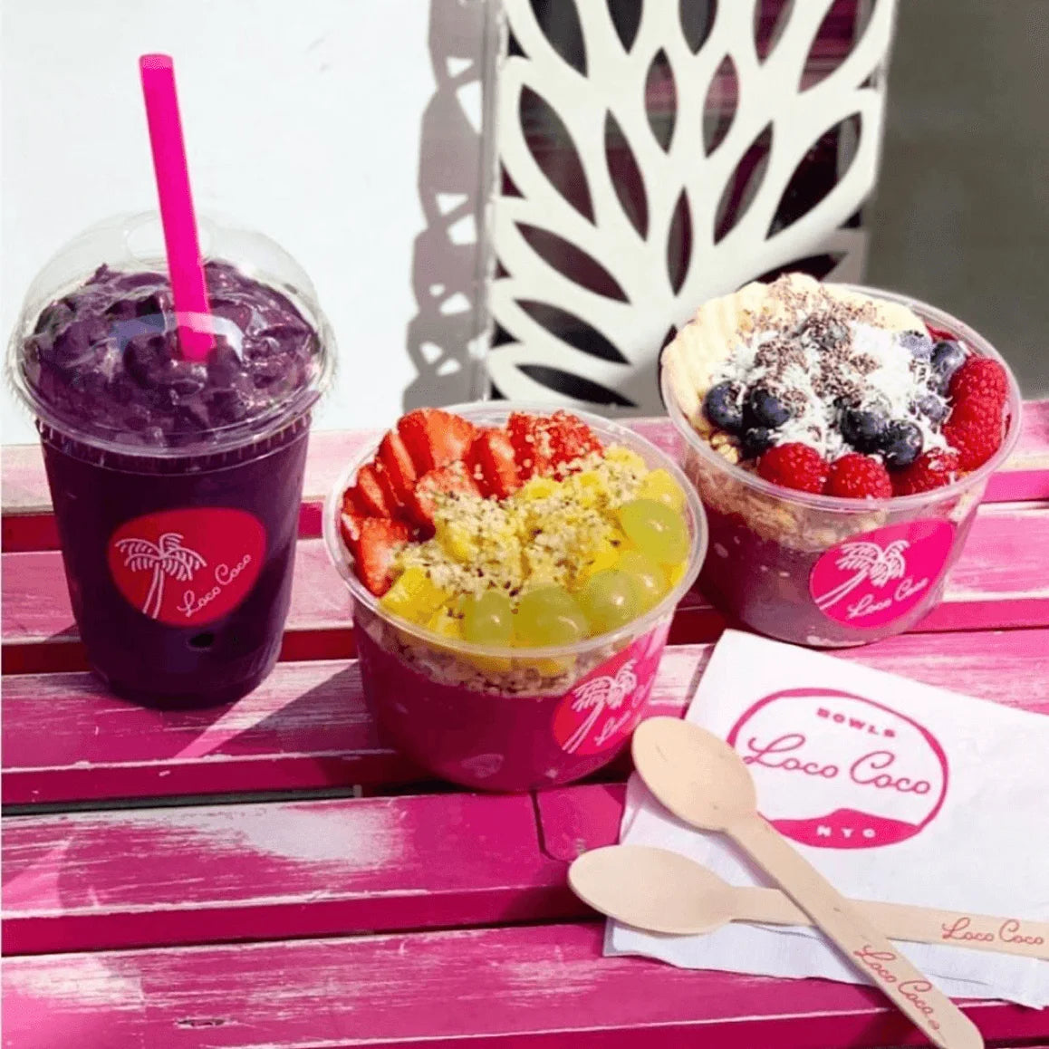Two fruit bowls and a purple drink with a pink straw on a pink surface, featuring the Loco Coco logo.