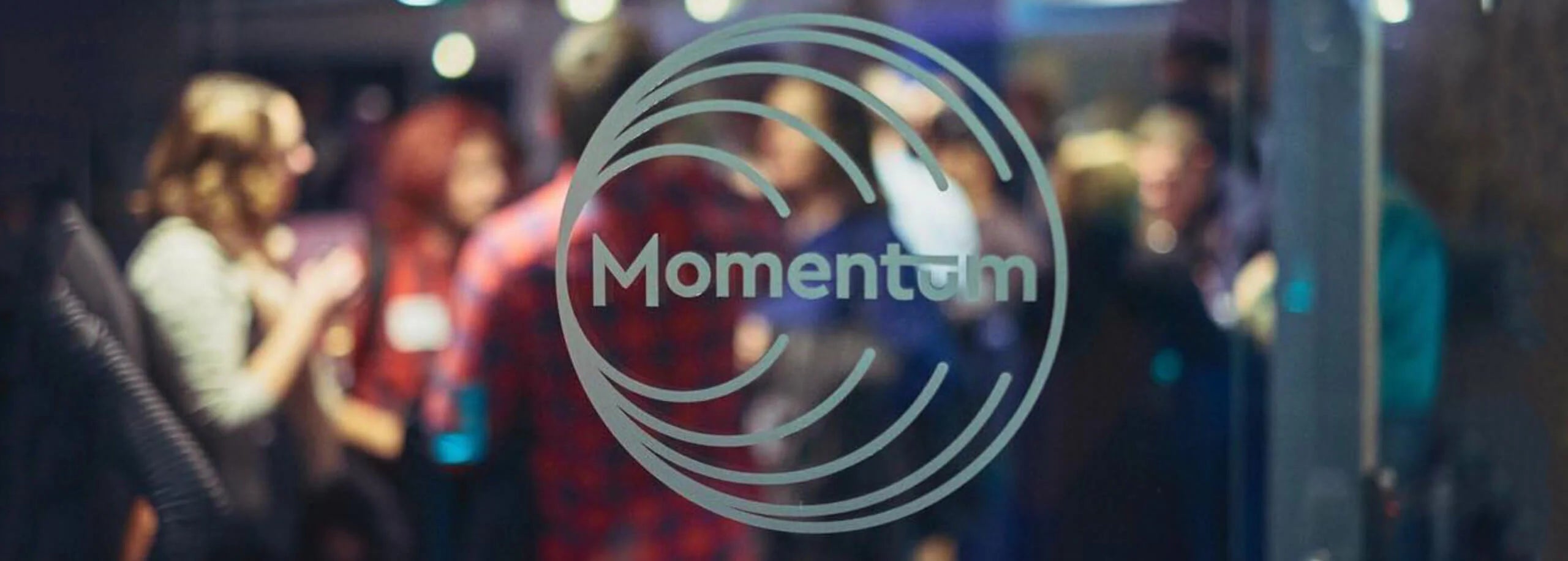 Blurred background of a crowd with 'Momentum' logo overlay