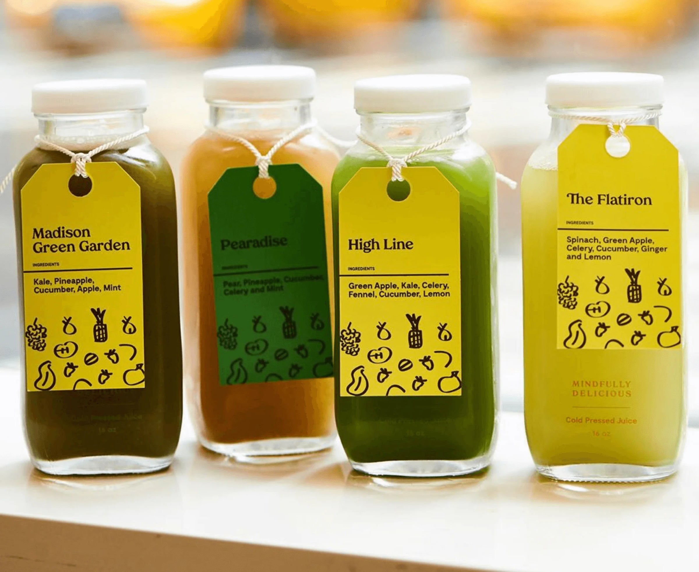 Four glass bottles of juice with colorful labels on a white surface.