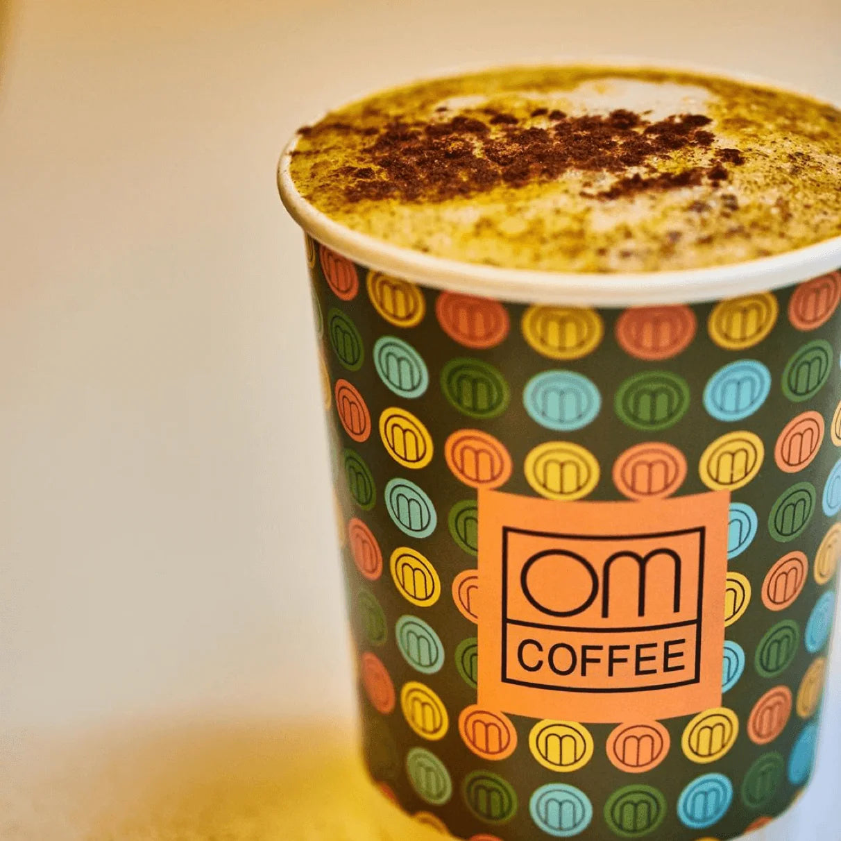 Colorful polka dot cup with 'OM Coffee' logo containing a coffee drink.
