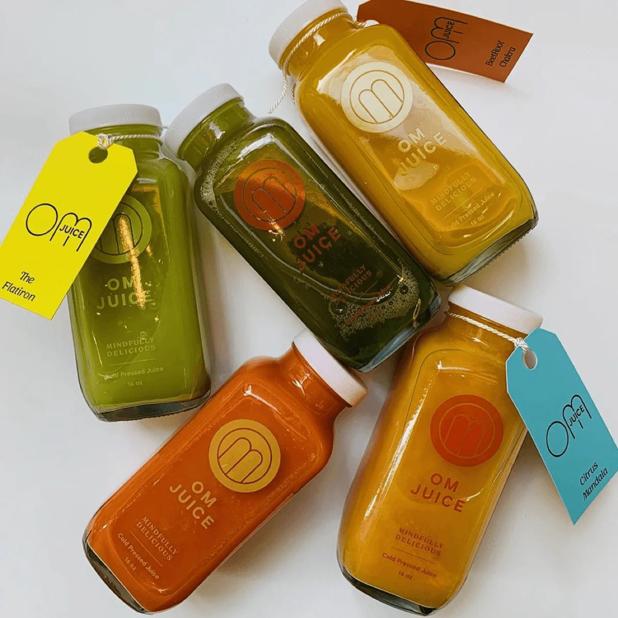 Five bottles of OM Juice on a white background with colorful tags.