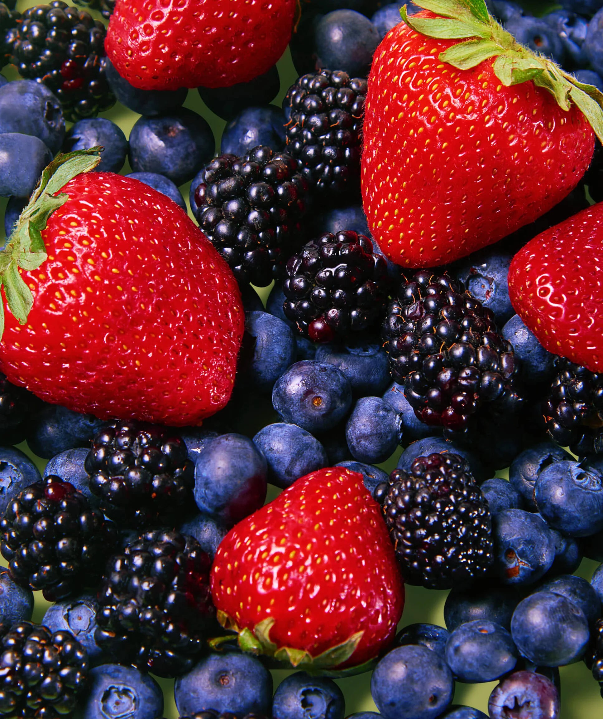 Assorted berries including strawberries, blueberries, and blackberries on a green surface.
