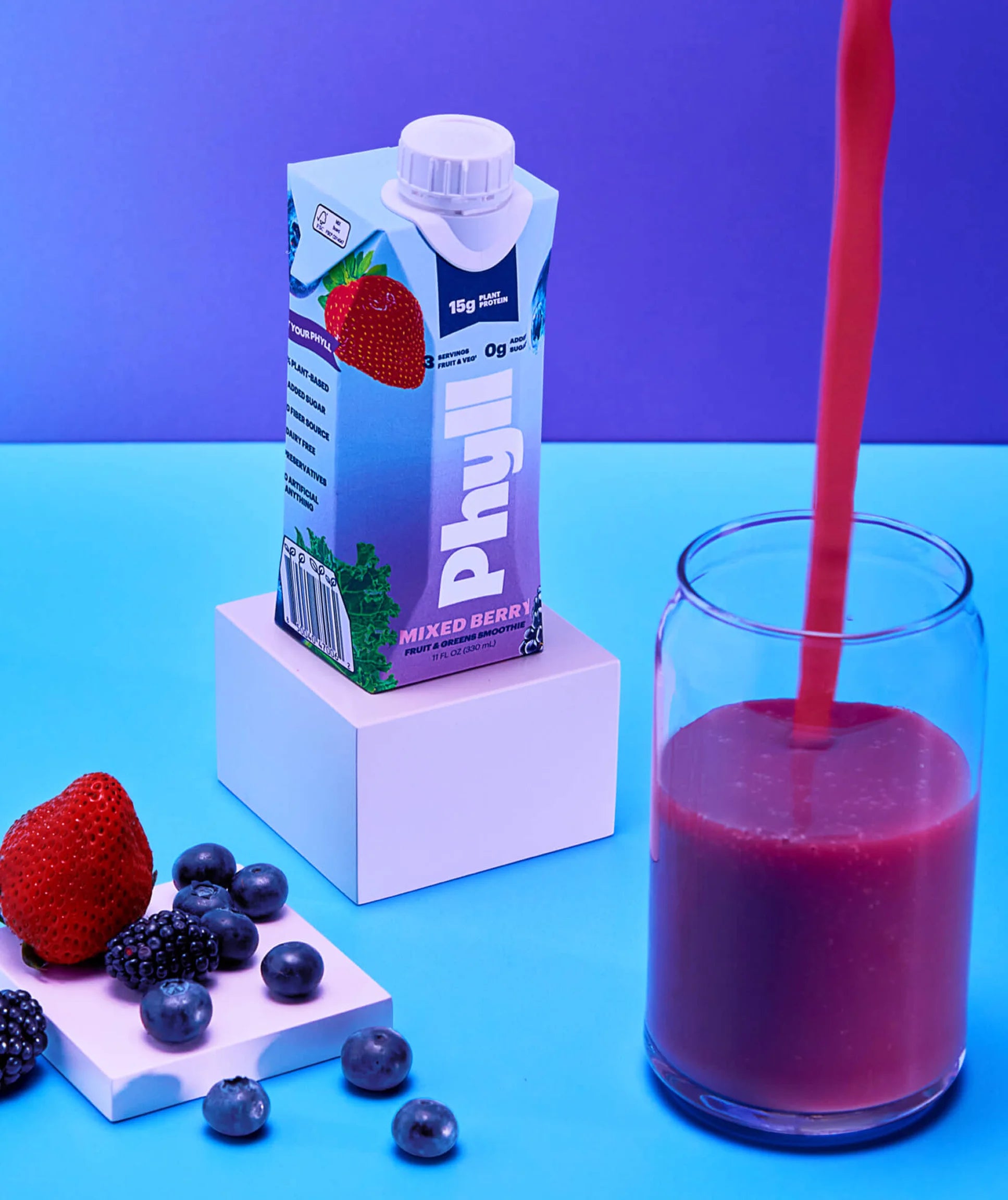 Phyff mixed berry juice being poured into a glass with berries on a blue background