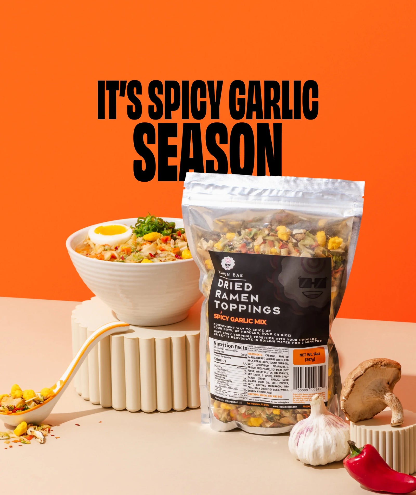 Spicy garlic ramen toppings package with a bowl of ramen and ingredients on an orange background.