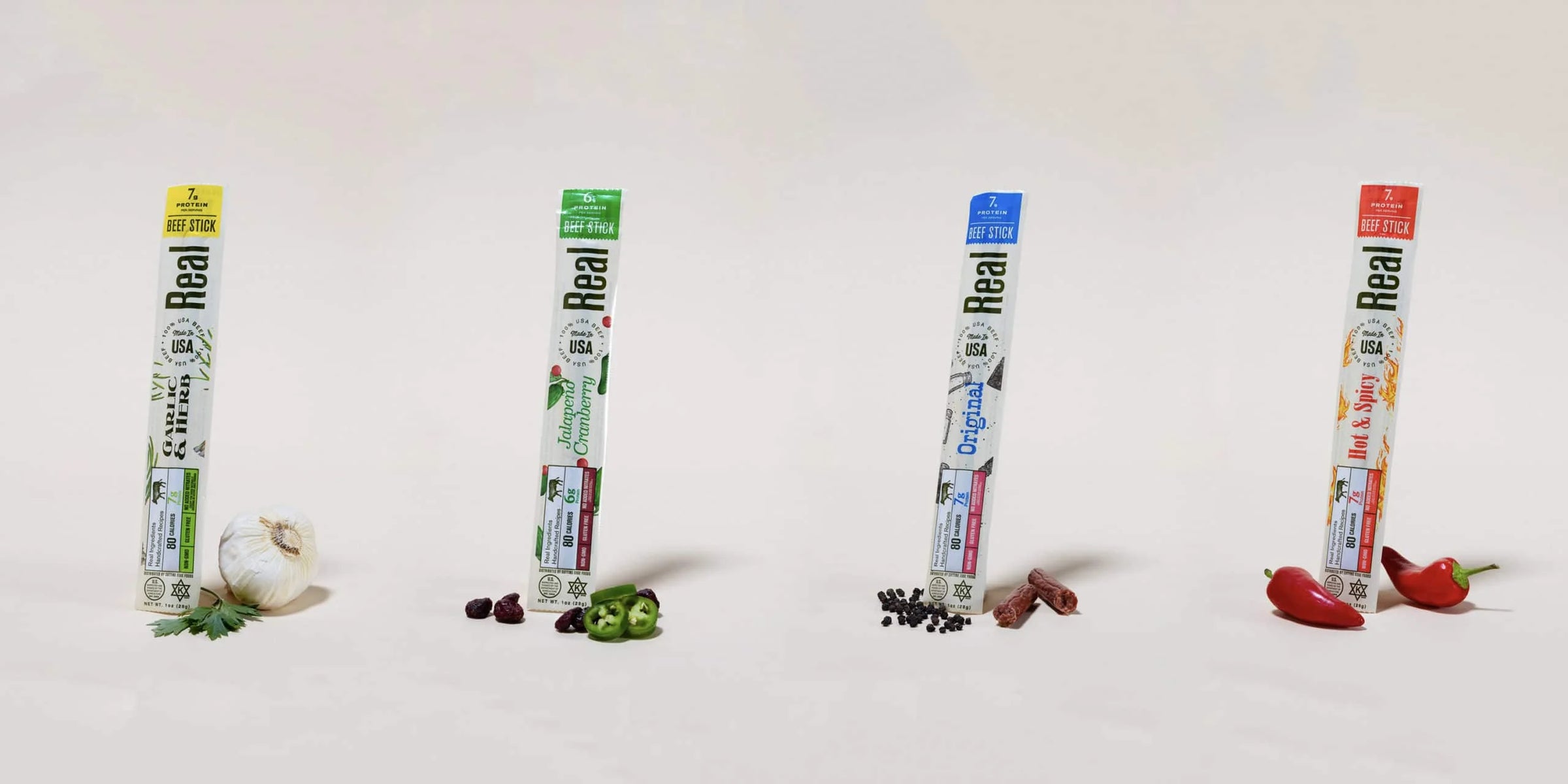 Four packages of Real Snacks beef sticks products on a white background with vegetables.