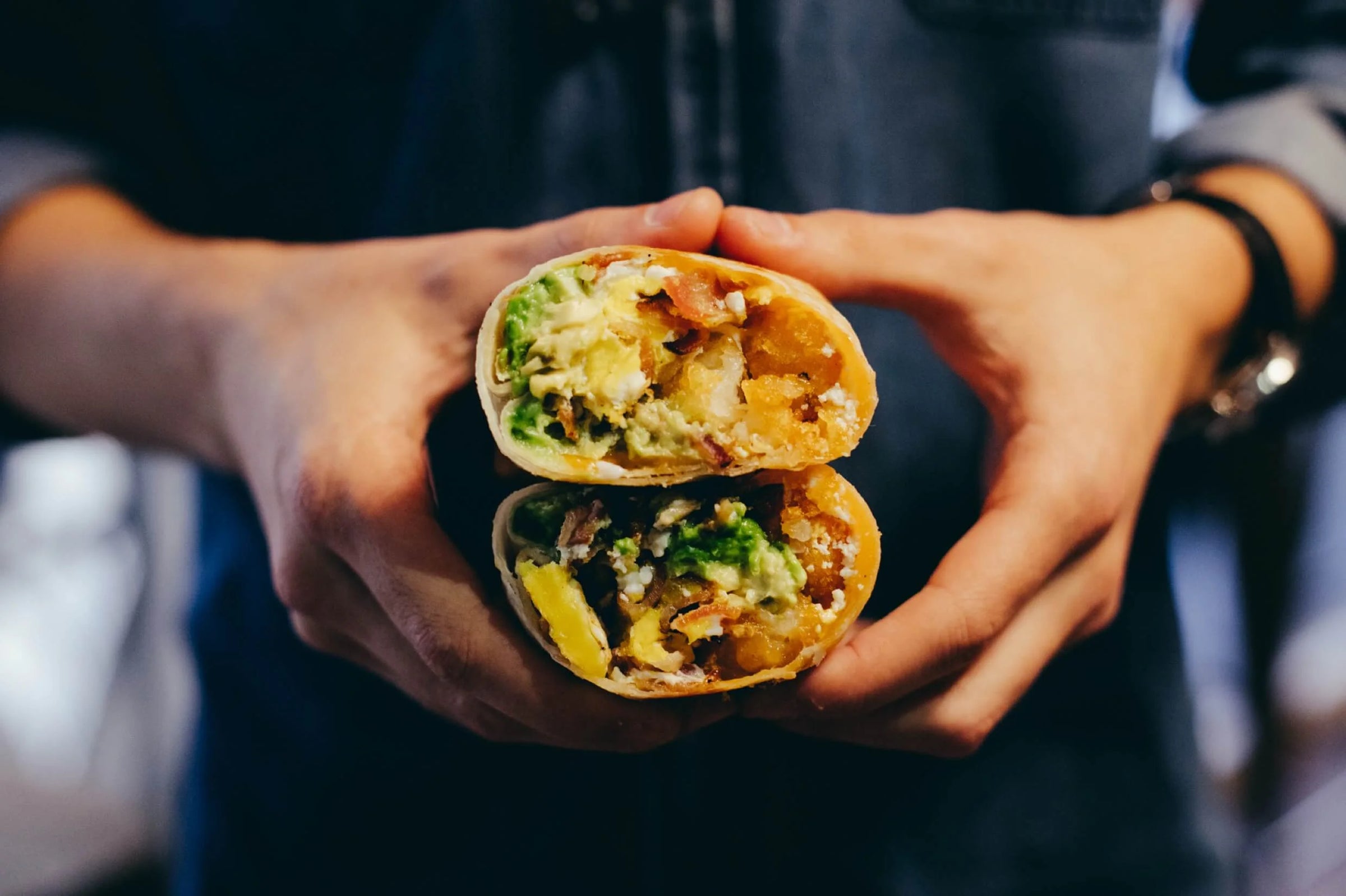 Person holding a halved burrito with visible ingredients