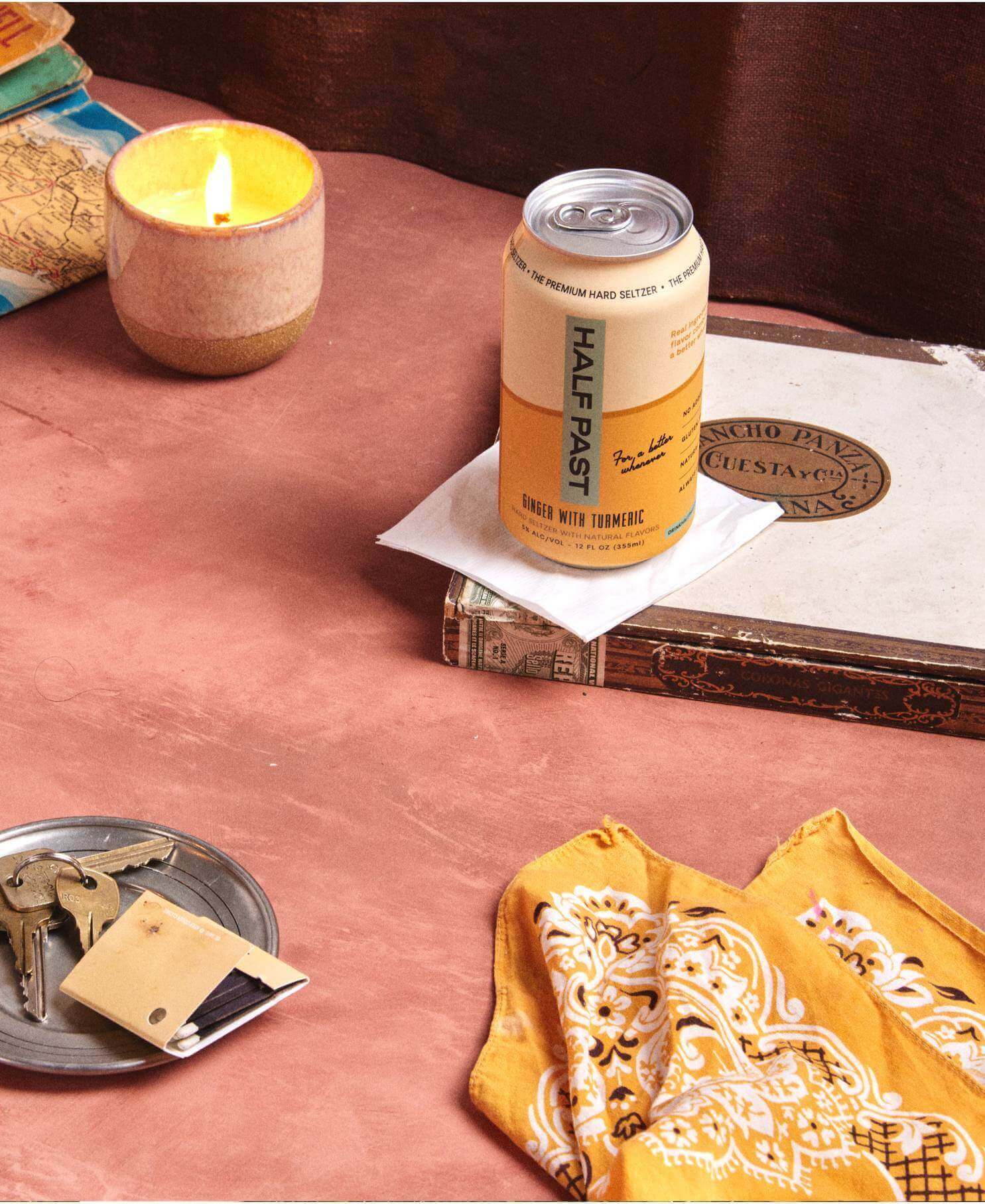 Lifestyle Photo of Ginger with Turmeric Flavored Half Past Hard Seltzer Can on a Table with a Candle and Bandana